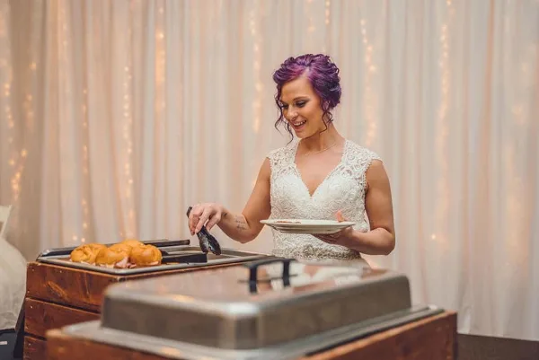 A catering buffet setup with chafing dishes and food, with a person serving themselves.