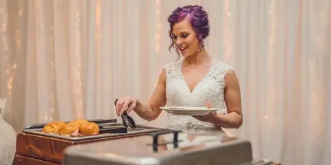 A catering buffet setup with chafing dishes and food, with a person serving themselves.