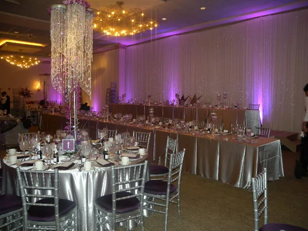 Interior of a banquet hall set up for a wedding reception with round tables, silver linens, and chandeliers.