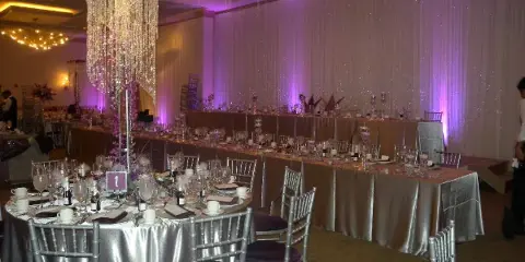 Interior of a banquet hall set up for a wedding reception with round tables, silver linens, and chandeliers.