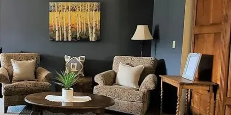 Interior lounge area of a lodge with upholstered armchairs, a coffee table, lamp, and wall art.