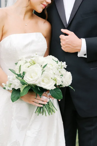 A bride in a white strapless gown holding a white bouquet standing next to a groom in a black tuxedo.