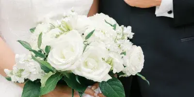 A bride in a white strapless gown holding a white bouquet standing next to a groom in a black tuxedo.