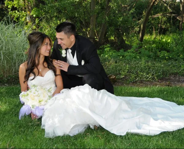 A bride and groom posing for a professional outdoor wedding portrait on a grassy lawn.