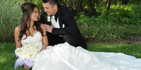 A bride and groom posing for a professional outdoor wedding portrait on a grassy lawn.