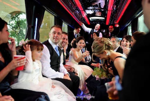 A bride and groom with guests riding inside a party bus during a wedding celebration.