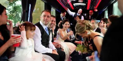 A bride and groom with guests riding inside a party bus during a wedding celebration.