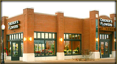 Exterior view of a brick Oberer's Flowers storefront with green window frames and floral displays in the windows.