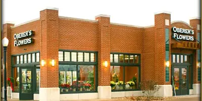 Exterior view of a brick Oberer's Flowers storefront with green window frames and floral displays in the windows.