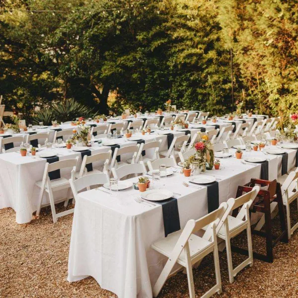 Outdoor event setup with rows of white folding chairs and tables covered in white linens and black runners.