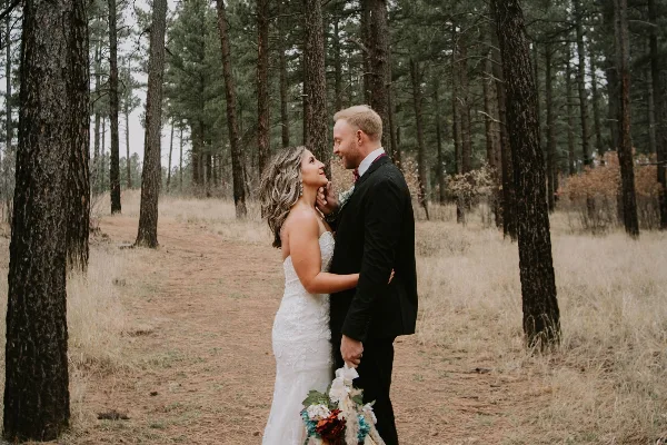 A bride and groom standing together in a pine forest setting.