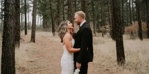 A bride and groom standing together in a pine forest setting.