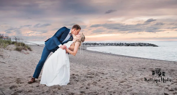 Wedding couple kissing on a sandy beach at sunset near the water.