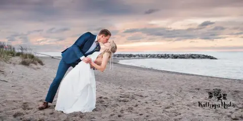 Wedding couple kissing on a sandy beach at sunset near the water.