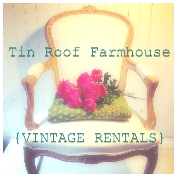 A vintage wooden armchair with white upholstery, featuring a green patterned cushion and a bouquet of pink flowers.