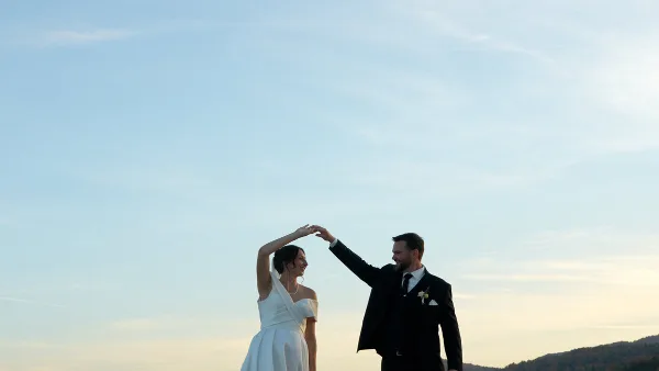 A bride and groom dancing outdoors against a clear blue sky.