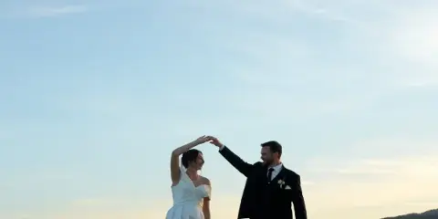 A bride and groom dancing outdoors against a clear blue sky.
