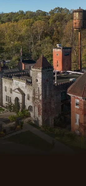 Aerial view of the historic Castle & Key distillery complex featuring stone buildings, a copper water tower, and surrounding wooded grounds.