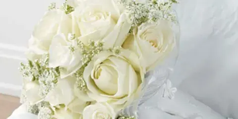 A white rose and baby's breath bouquet resting on a white bed.