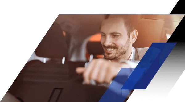 A smiling professional driver sitting in the driver's seat of a car, holding the steering wheel.