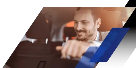 A smiling professional driver sitting in the driver's seat of a car, holding the steering wheel.