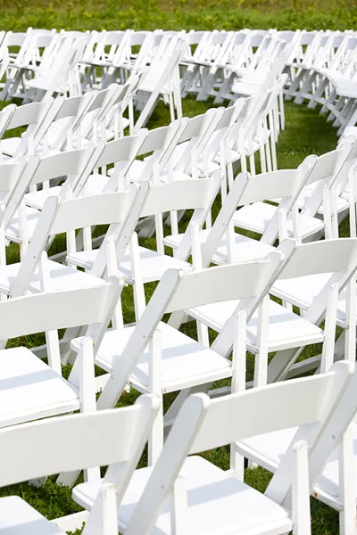 Rows of white folding chairs arranged on grass for an outdoor event.