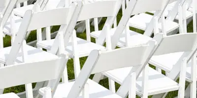 Rows of white folding chairs arranged on grass for an outdoor event.