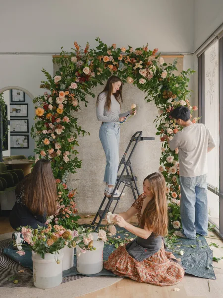 Floral designers assembling a large, custom floral arch in a studio.