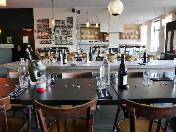 Interior view of a restaurant dining room with wooden tables, chairs, and a bar area in the background.