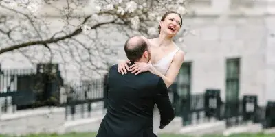 A bride and groom laughing together outdoors near a blooming tree.