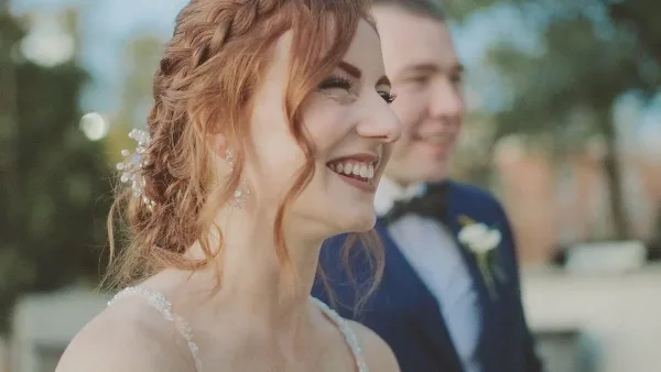 A smiling bride with red hair and a groom in a suit, captured in a cinematic close-up style.