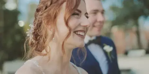 A smiling bride with red hair and a groom in a suit, captured in a cinematic close-up style.