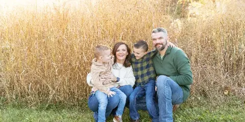 A family of four posing together in a field of tall golden grass.