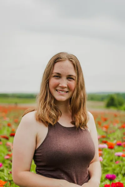 Portrait of a smiling woman with reddish-brown hair standing in a field of flowers.