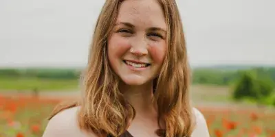 Portrait of a smiling woman with reddish-brown hair standing in a field of flowers.