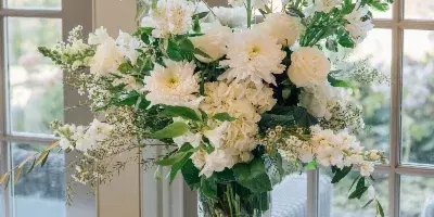 A tall white floral centerpiece in a glass vase sitting on a table with place cards.
