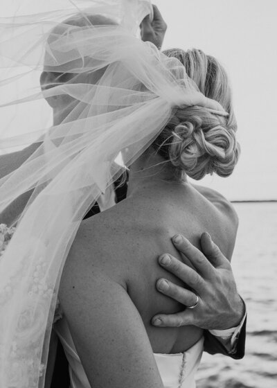 Black and white photo of a bride and groom embracing, showing the groom's hand on the bride's back and a wedding ring.