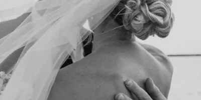 Black and white photo of a bride and groom embracing, showing the groom's hand on the bride's back and a wedding ring.