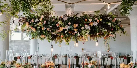 A large, lush floral installation with hanging greenery and mixed flowers suspended above a long event table.