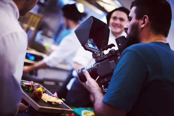 A videographer filming a scene in a kitchen using a professional camera.