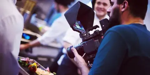A videographer filming a scene in a kitchen using a professional camera.