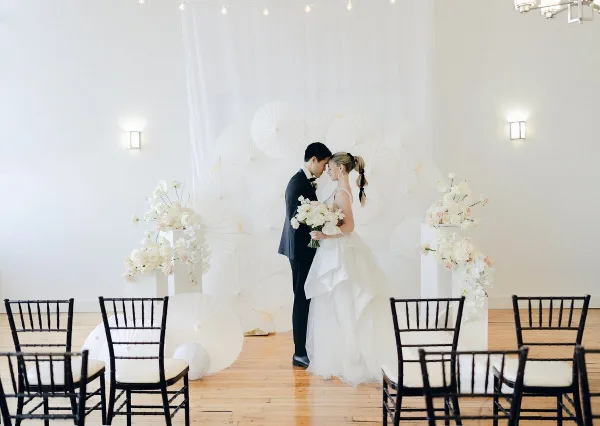 A bride and groom standing at a wedding ceremony altar decorated with white parasols and floral arrangements.
