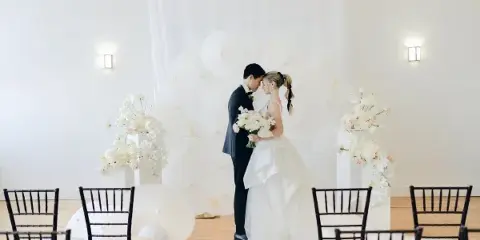A bride and groom standing at a wedding ceremony altar decorated with white parasols and floral arrangements.