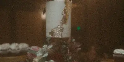 A two-tier white wedding cake decorated with gold leaf and fresh flowers, topped with a 'Mr & Mrs' topper, displayed on a stand with cupcakes in the background.