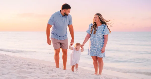 A family of three walking on a sandy beach at sunset.