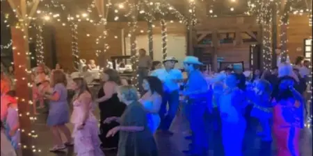 Packed wedding dance floor with guests dancing under string lights