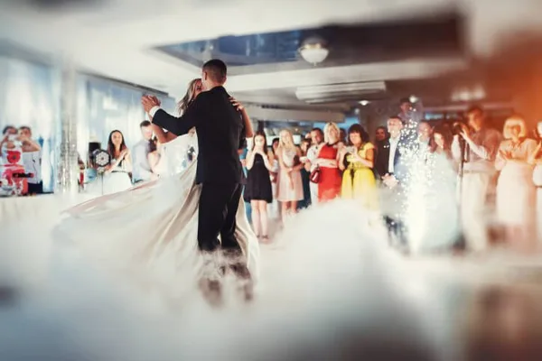 A couple shares a first dance at a wedding reception while guests watch and confetti falls in the venue.