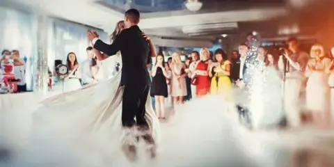 A couple shares a first dance at a wedding reception while guests watch and confetti falls in the venue.