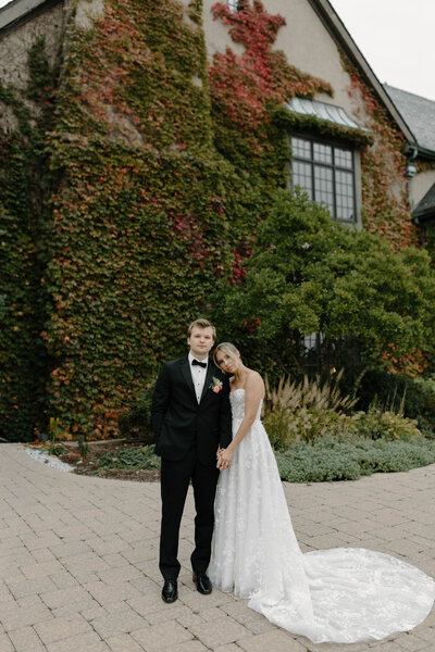 A bride and groom standing together in front of an ivy-covered building.