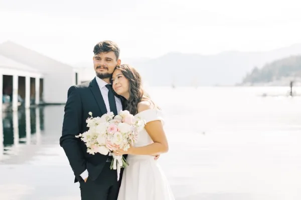 A bride and groom standing together, with the bride holding a large bouquet of white and pink flowers.